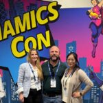 Christina Korff, Stefan Falkenhagen und Linh Schmidt stehen vor einem Banner der DynamicsCon 2025 und blicken in die Kamera