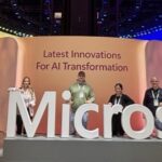 Vier Sven Mahn IT Mitarbeiterinnen und Mitarbeiter stehen hinter einem großen Microsoft-Slogan auf der Microsoft Ignite 2024